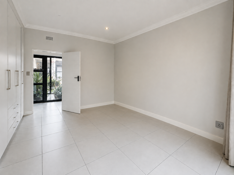 A bright, empty bedroom featuring neutral tiled flooring, built-in cupboards, and clean finishes, offering a versatile space ready for personalization.