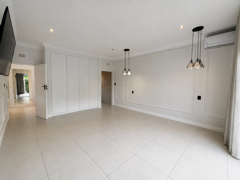 Spacious, modern living area featuring neutral tiled flooring, elegant wall moulding, built-in cabinetry, and contemporary pendant lighting.