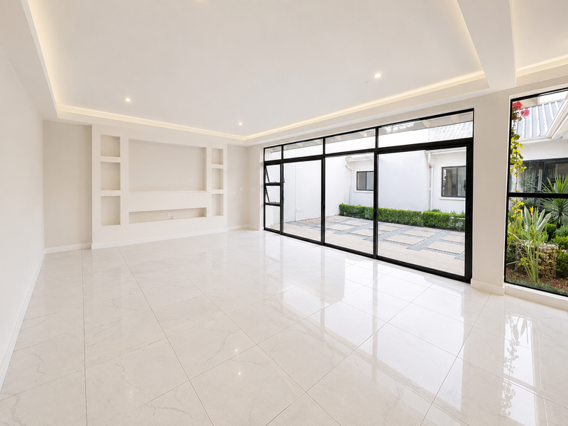 Spacious, modern living area featuring large format porcelain tiles, recessed cove lighting, and expansive black aluminium sliding doors opening to a private courtyard.