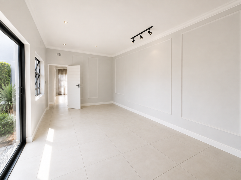 A bright, empty living area featuring elegant wainscoting, modern track lighting, and large sliding glass doors that open to a private garden space.