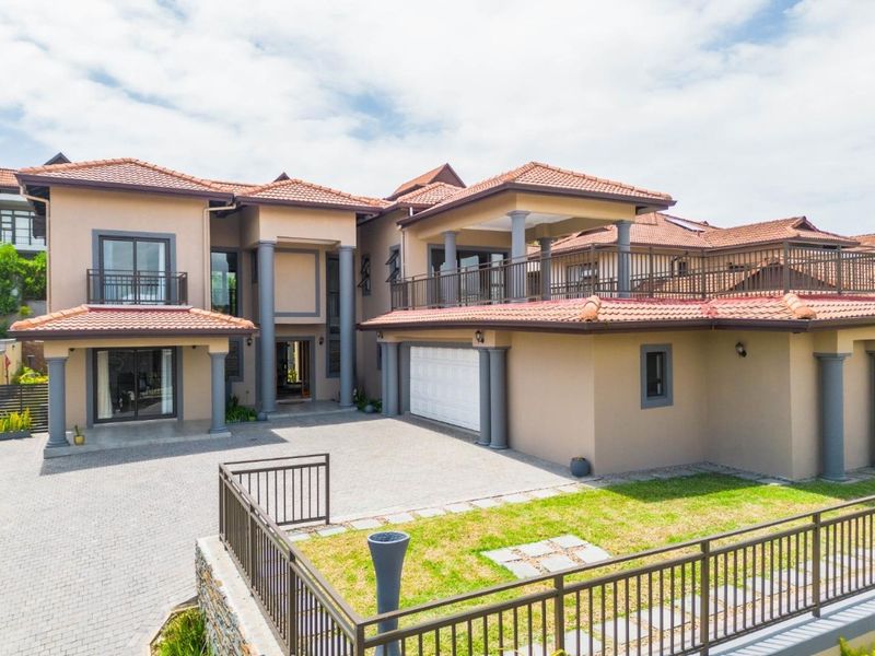 A spacious multi-level residence featuring a paved driveway, double garage, and an expansive upper-level balcony with classic architectural columns.