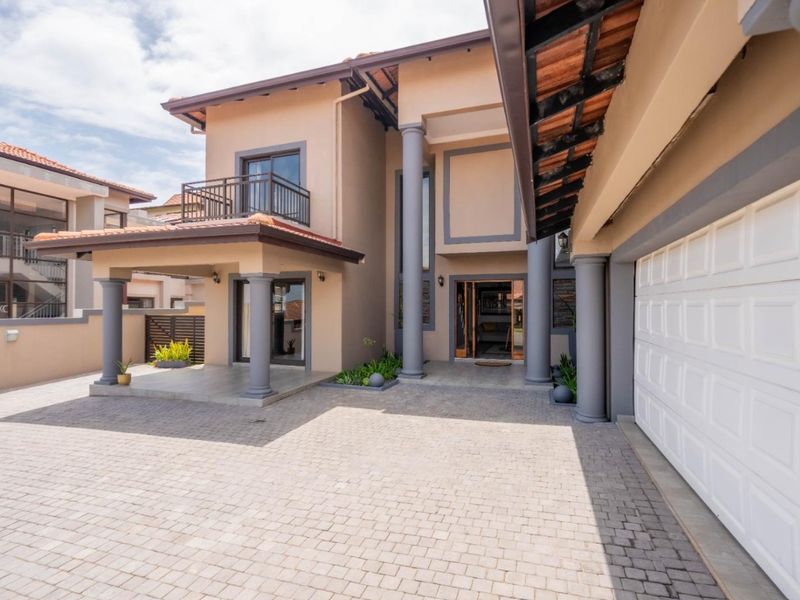 A well-maintained double-story home featuring a paved driveway, double garage, covered entrance porch, and an upper-level balcony.