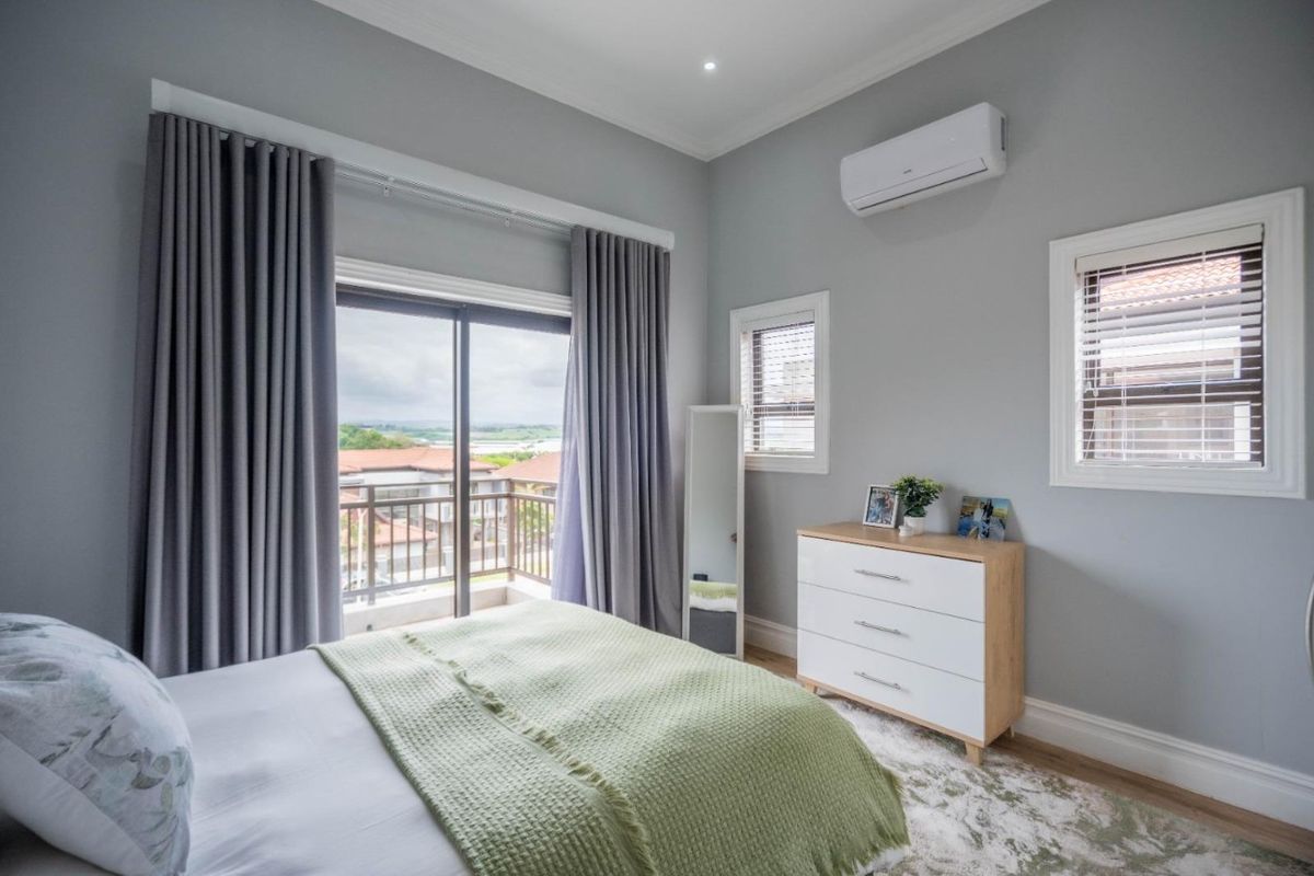 A well-maintained bedroom featuring neutral grey walls, air conditioning, and a sliding glass door providing access to a private balcony with scenic views.