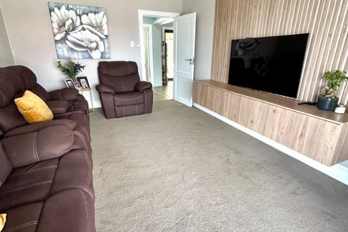 A comfortable living room featuring a modern timber slat feature wall with a floating media console and neutral carpeting.
