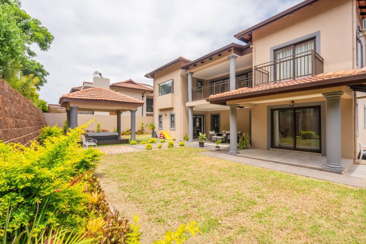 Spacious rear exterior featuring a landscaped garden, covered patio, upper-level balcony, and a detached gazebo, ideal for outdoor entertaining.