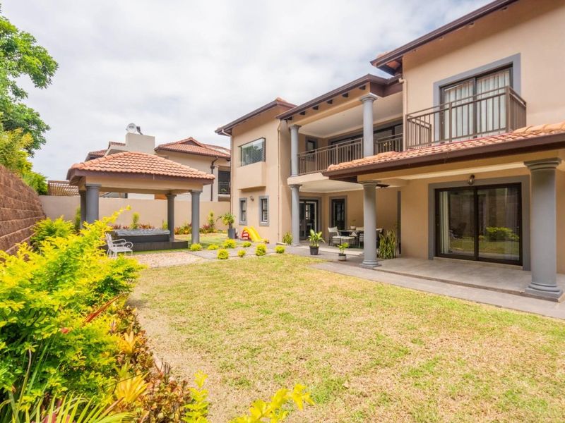 Spacious rear exterior featuring a landscaped garden, covered patio, upper-level balcony, and a detached gazebo, ideal for outdoor entertaining.