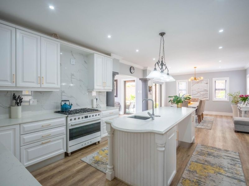Spacious open-plan kitchen and dining area featuring a central island, modern gas stove, marble-look splashback, and high-quality finishes throughout.