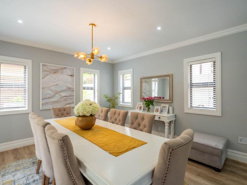 A bright and well-maintained dining room featuring crown molding, recessed downlights, and timber-look flooring, creating an elegant space for formal dining.