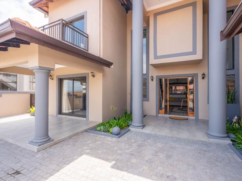 A well-maintained front entrance featuring a paved driveway, covered patio area, decorative columns, and a balcony overlooking the main entryway.
