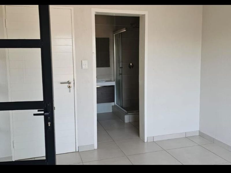 A clean, modern bedroom featuring neutral tiled flooring and a convenient en-suite bathroom with a glass shower enclosure.