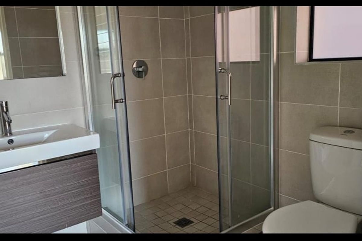 A modern bathroom featuring a vanity with basin, a glass-enclosed shower, and a toilet, finished with neutral wall and floor tiles.