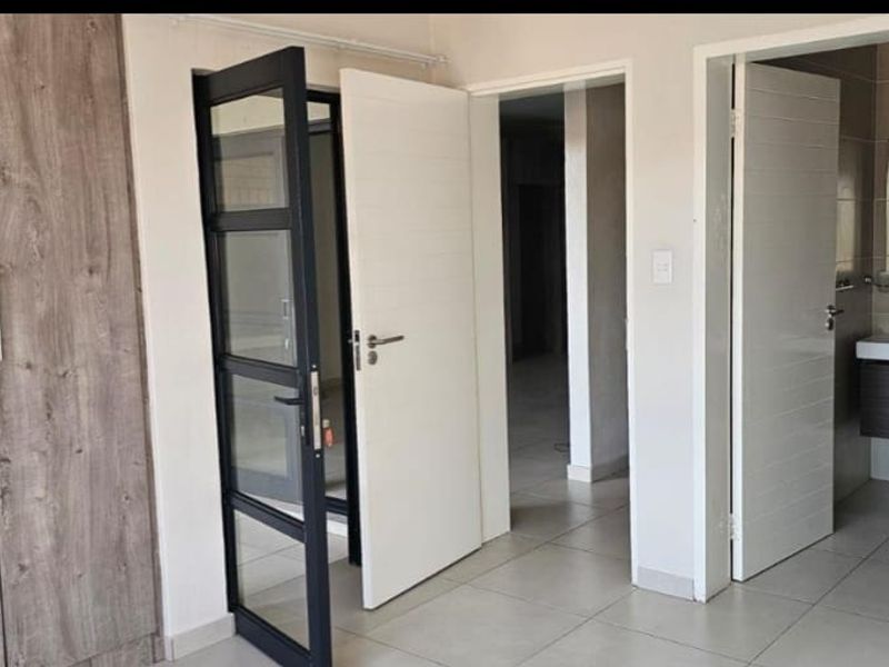 A clean, modern bedroom featuring built-in wood-grain cupboards, tiled flooring, and direct access to an en-suite bathroom.