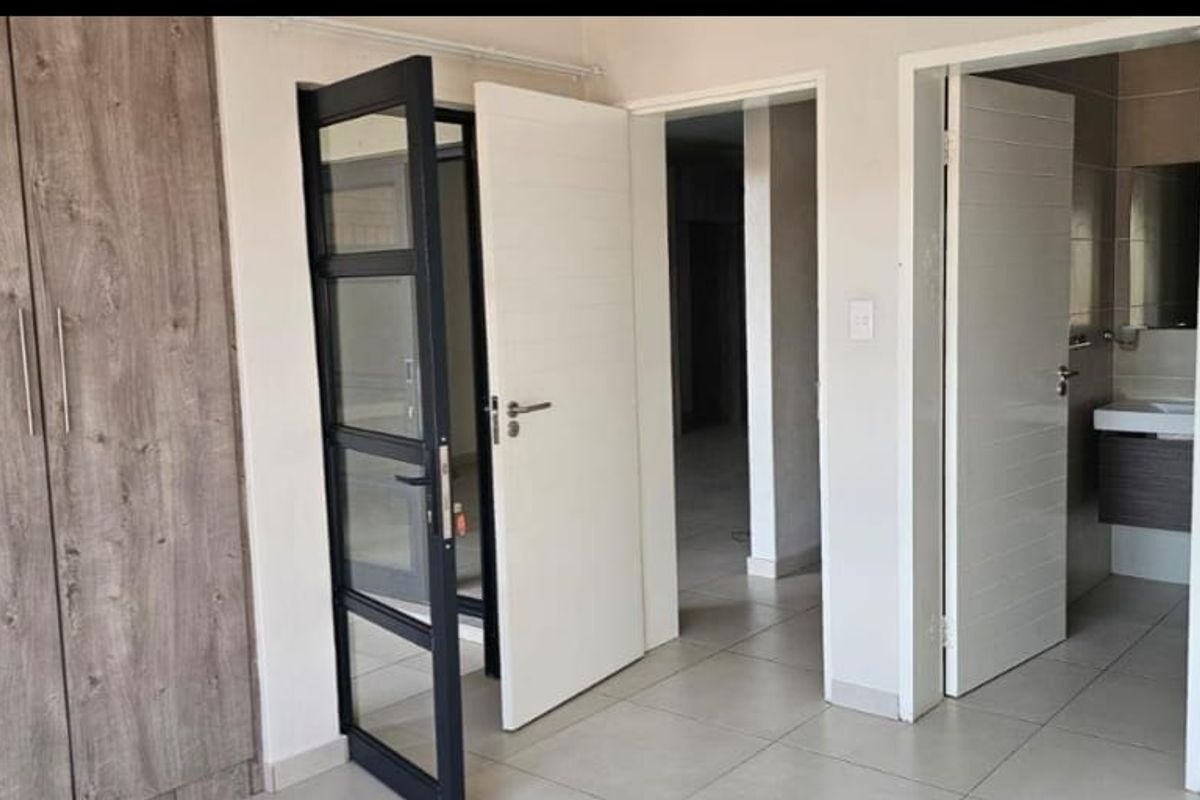A clean, modern bedroom featuring built-in wood-grain cupboards, tiled flooring, and direct access to an en-suite bathroom.