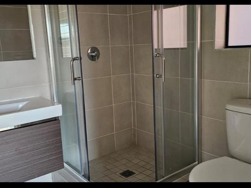 A modern bathroom featuring a vanity with basin, a glass-enclosed shower, and a toilet, finished with neutral wall and floor tiles.