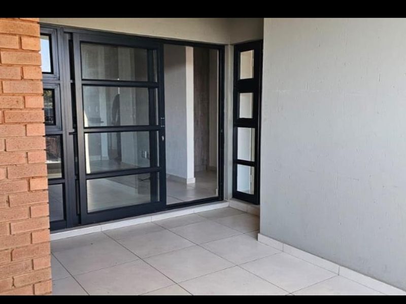 A clean, modern balcony featuring tiled flooring, an exposed brick feature wall, and large sliding glass doors leading into the apartment interior.