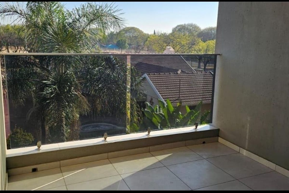A clean, modern balcony featuring a frameless glass balustrade and tiled flooring, offering an open view of the surrounding neighborhood.