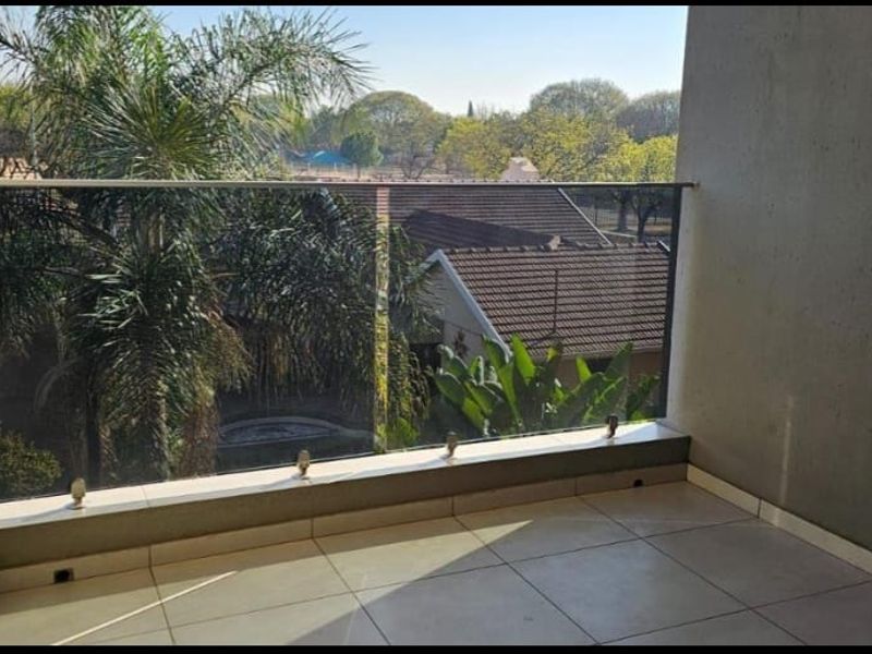 A clean, modern balcony featuring a frameless glass balustrade and tiled flooring, offering an open view of the surrounding neighborhood.