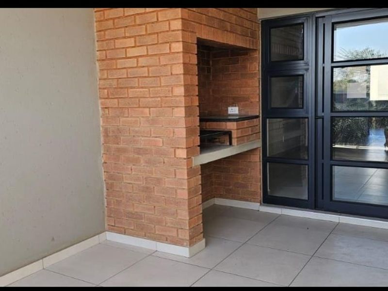 Covered patio area featuring a built-in brick braai, tiled flooring, and large aluminium sliding doors providing access to the interior.