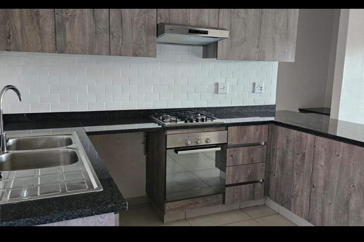 Modern kitchen featuring wood-grain cabinetry, granite countertops, subway tile backsplash, and integrated stainless steel appliances including a gas hob and oven.