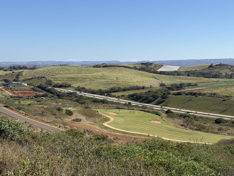 Elevated panoramic view overlooking a golf course, surrounding green hills, and a nearby highway.