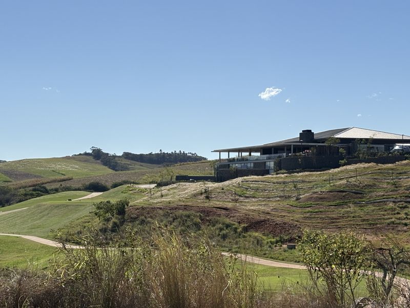 A scenic view of a residential property set within a rolling landscape, featuring manicured grounds, stone retaining walls, and paved access paths.