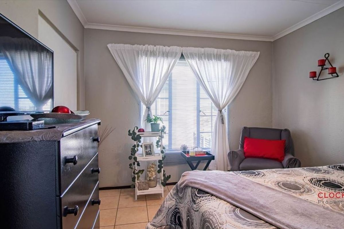 A functional bedroom featuring tiled flooring, neutral wall tones, and window treatments including venetian blinds and curtains.