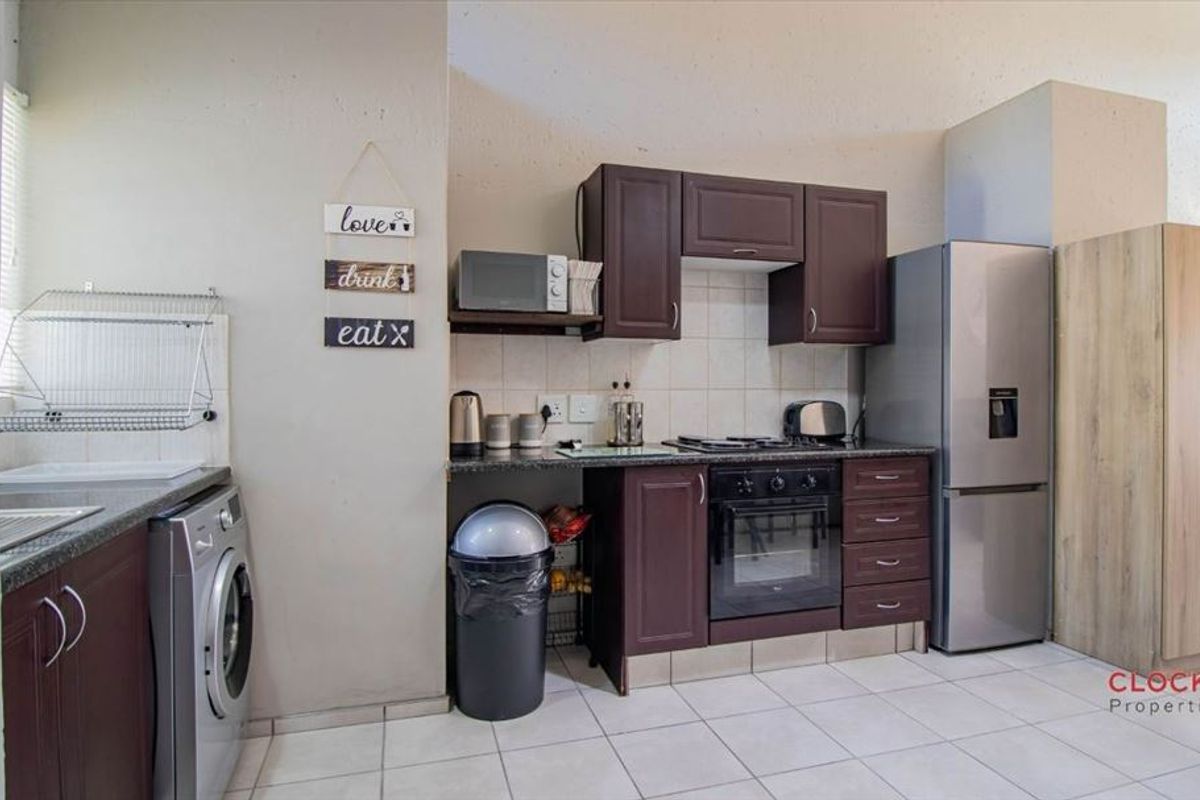 A functional kitchen featuring dark wood cabinetry, granite countertops, a built-in oven, gas hob, and tiled flooring with space for laundry appliances.