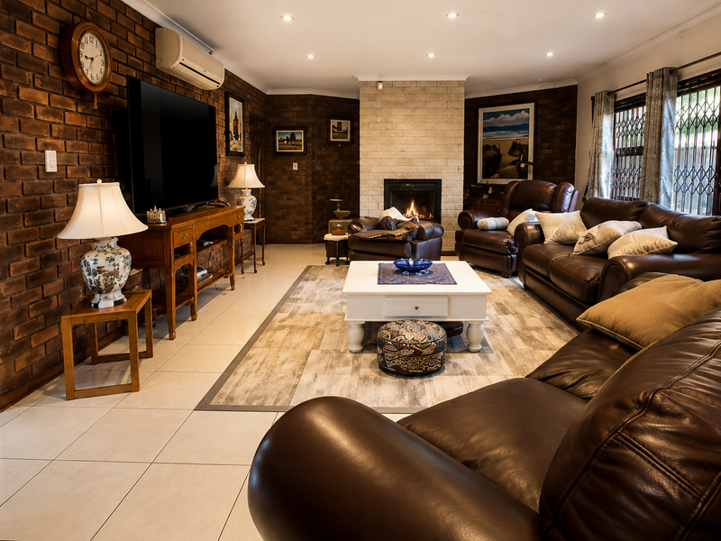 Spacious living room featuring an exposed brick wall, a stone fireplace, tiled flooring, and recessed lighting, creating a warm and inviting atmosphere.