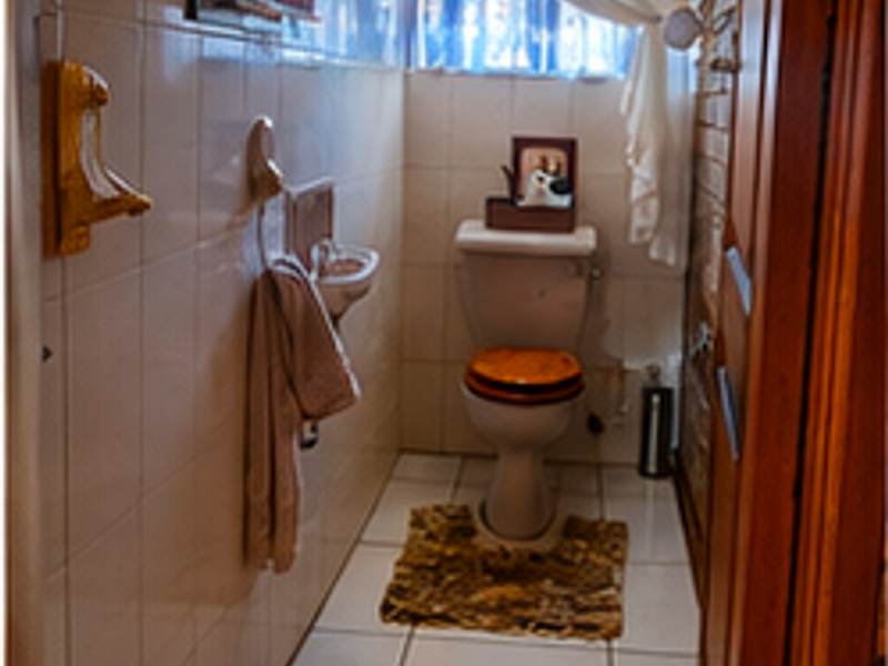 A compact bathroom featuring ceramic wall and floor tiles, a wall-mounted basin, and a standard toilet with a security gate on the window.