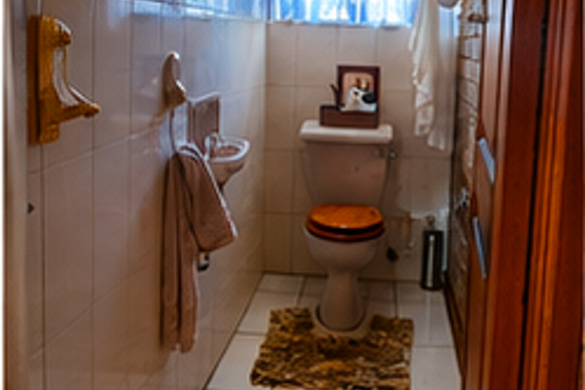 A compact bathroom featuring ceramic wall and floor tiles, a wall-mounted basin, and a standard toilet with a security gate on the window.