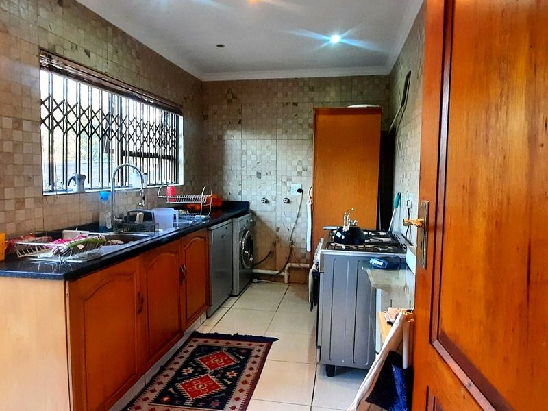 A functional kitchen featuring wooden cabinetry, granite countertops, tiled backsplash, and a freestanding stove, with a window fitted with a security gate.