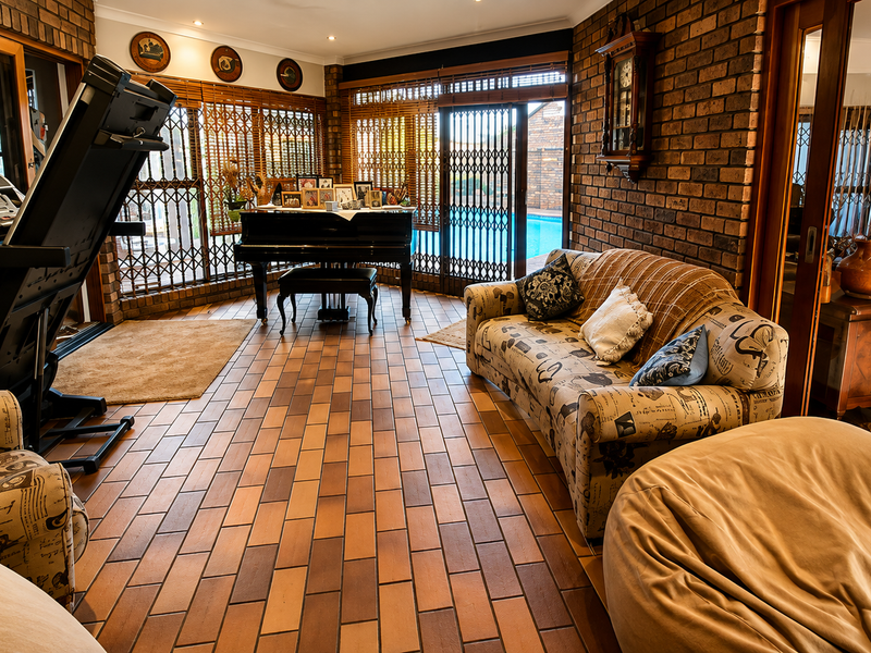Spacious living area featuring exposed brick walls, terracotta tile flooring, and large sliding glass doors with security gates providing access to the pool area.