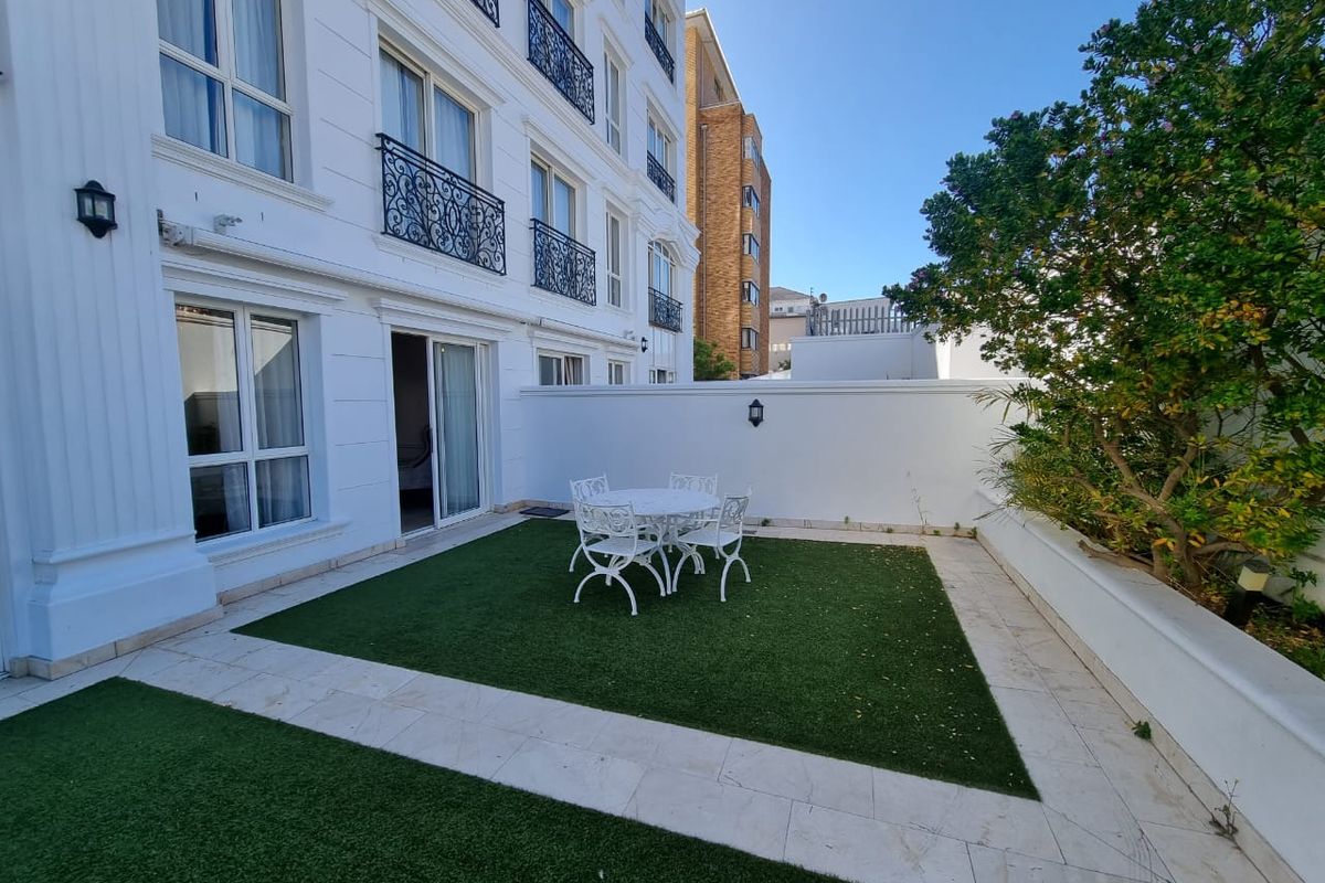 A well-maintained ground floor patio featuring artificial turf, stone paving, and direct access to the apartment through sliding glass doors.