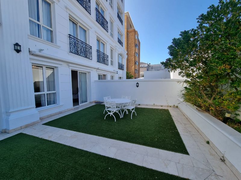 A well-maintained ground floor patio featuring artificial turf, stone paving, and direct access to the apartment through sliding glass doors.