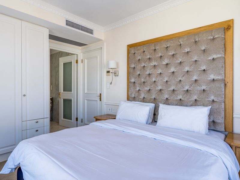 A well-appointed bedroom featuring a tufted upholstered headboard, built-in cabinetry, crown molding, and integrated ducted air conditioning with an en-suite bathroom access.