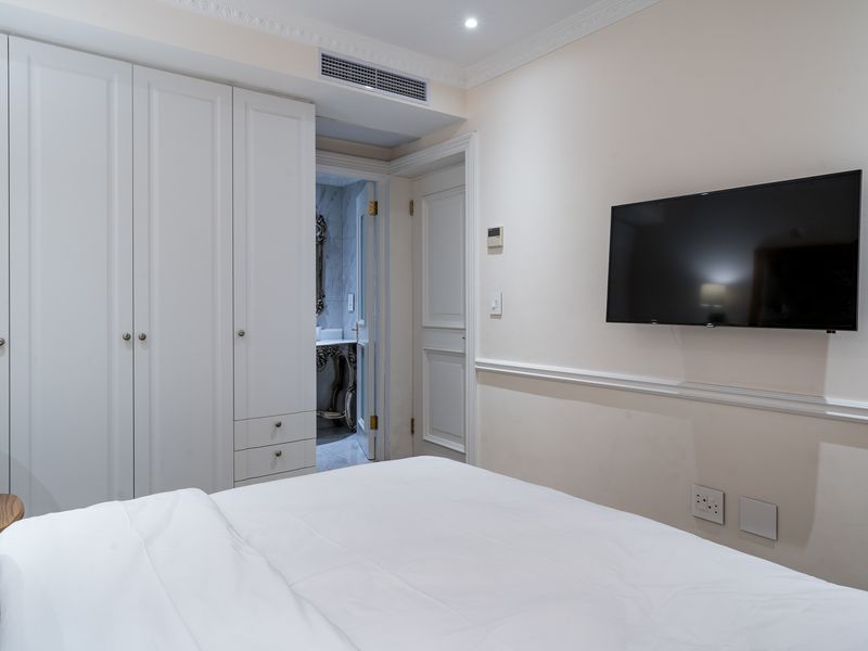 A well-maintained bedroom featuring built-in cupboards, crown molding, and ducted air conditioning, with an adjoining bathroom visible through the doorway.