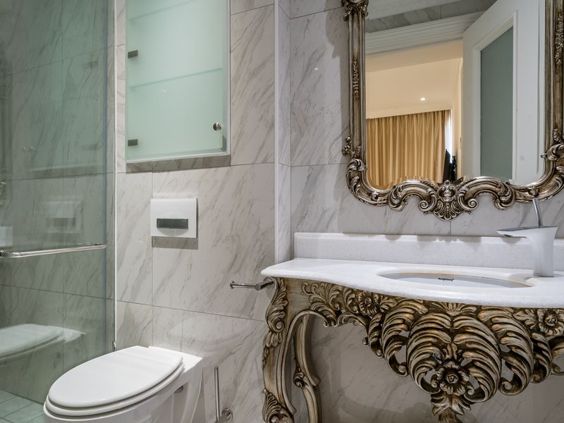 Modern bathroom featuring marble wall tiling, a glass shower enclosure, a wall-mounted toilet, and an ornate vanity with a marble countertop.