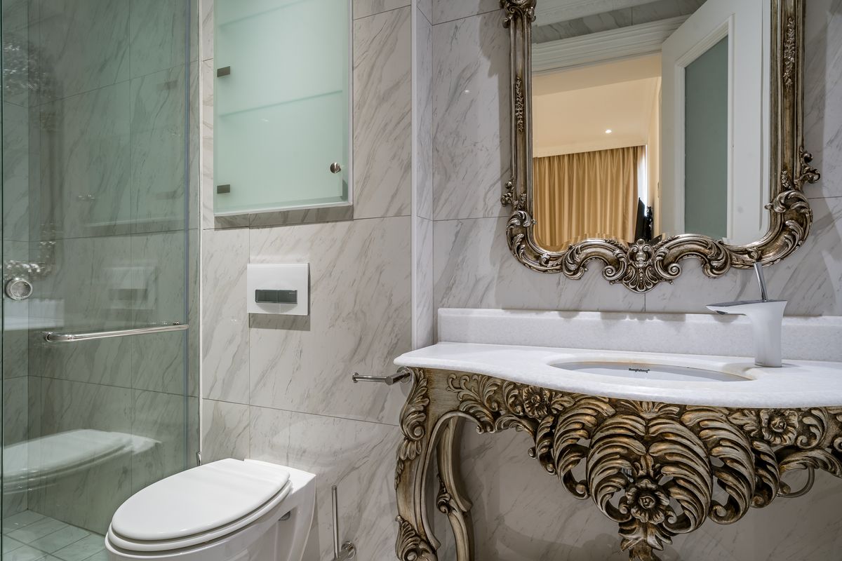 Modern bathroom featuring marble wall tiling, a glass shower enclosure, a wall-mounted toilet, and an ornate vanity with a marble countertop.