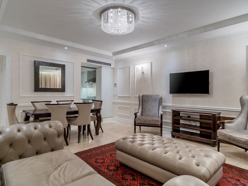 Elegant open-plan living and dining area featuring sophisticated wainscoting, crown molding, stone flooring, and a striking crystal chandelier.