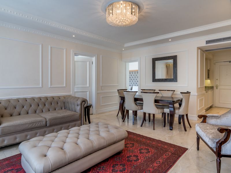 Elegant open-plan living and dining area featuring sophisticated wainscoting, crown molding, polished marble flooring, and a grand crystal chandelier.