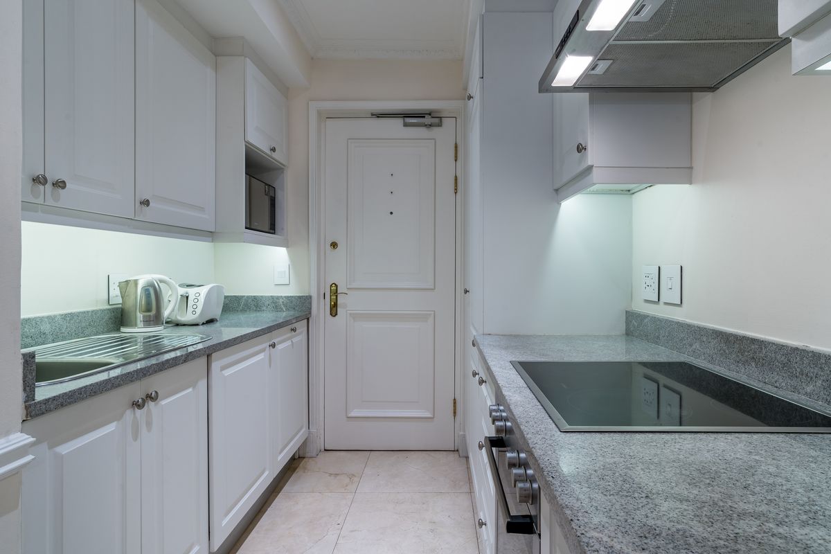 A well-maintained galley kitchen featuring granite countertops, built-in cabinetry, an integrated oven, and an electric hob with an overhead extractor fan.