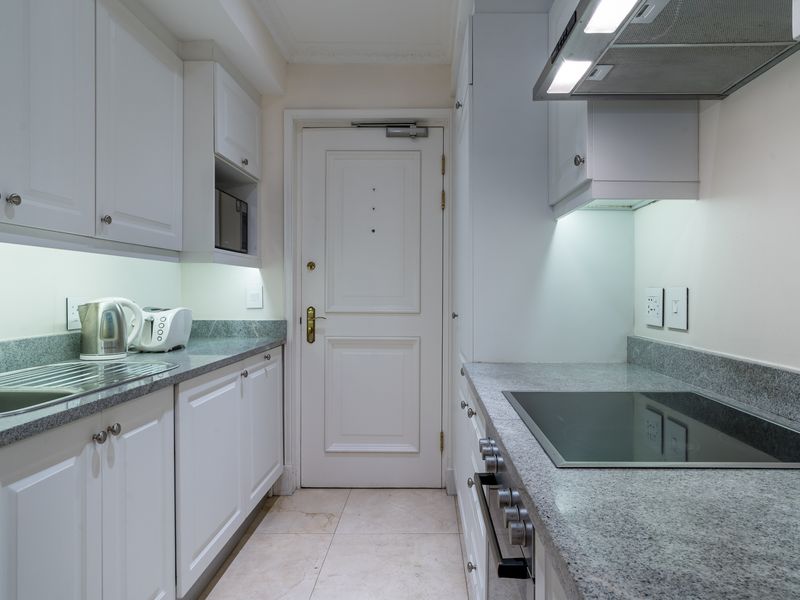 A well-maintained galley kitchen featuring granite countertops, built-in cabinetry, an integrated oven, and an electric hob with an overhead extractor fan.