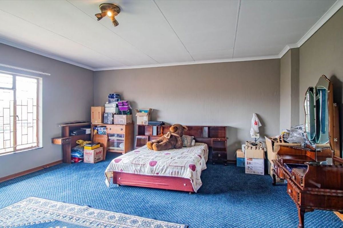 Spacious bedroom featuring blue carpeting, large window with security bars, and a central ceiling light fixture.