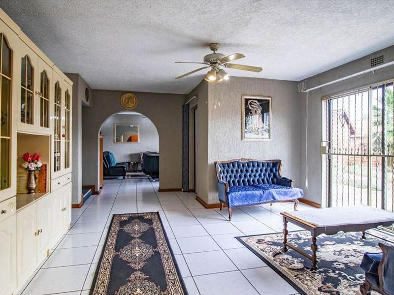 Spacious living room featuring tiled flooring, built-in cabinetry, a ceiling fan, and a sliding glass door with security gate leading to the exterior.
