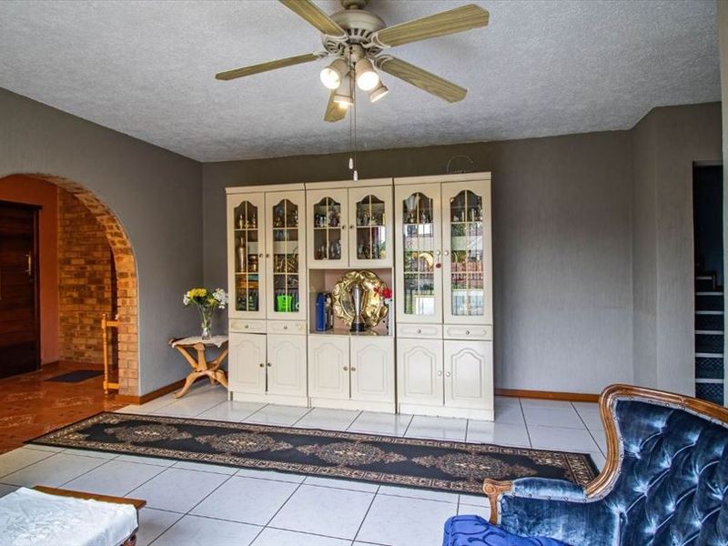 Spacious living room featuring tiled flooring, a central ceiling fan, and a distinctive brick archway leading to an adjacent area.