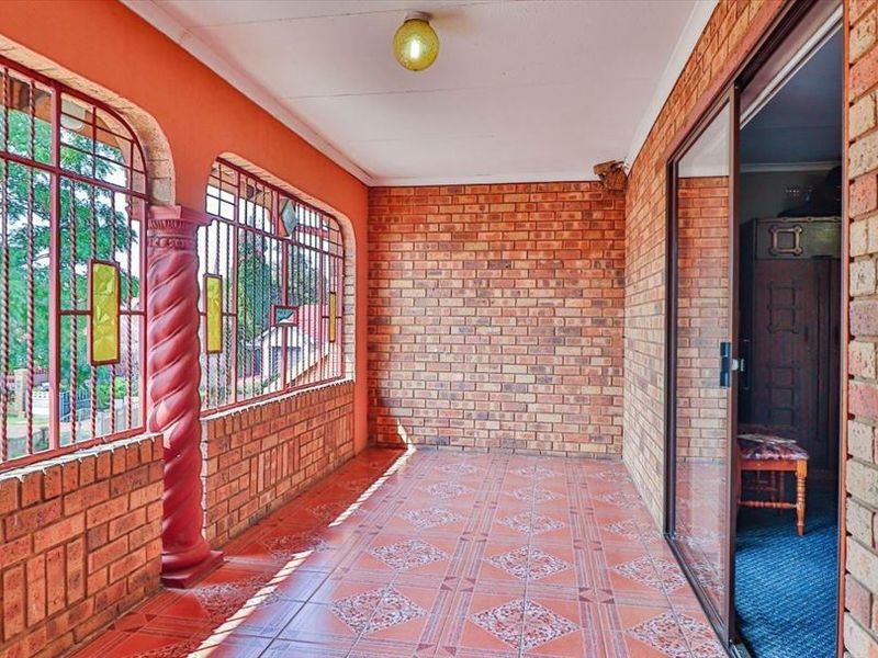 A covered patio area featuring exposed brick walls, decorative pillars, security bars, and tiled flooring, providing a functional outdoor space.