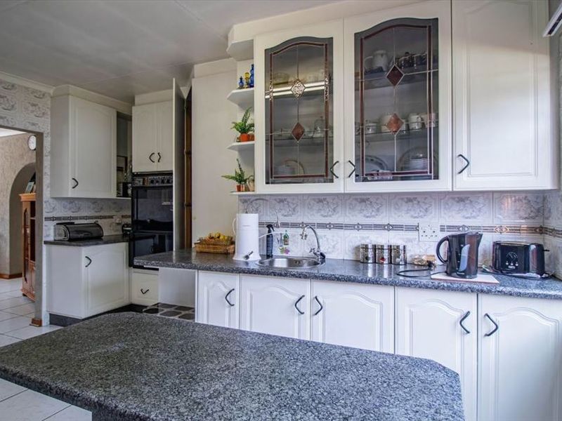 A functional kitchen featuring white cabinetry, granite countertops, a built-in oven, and a tiled backsplash, with an adjacent dining area visible.