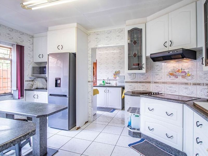 A functional kitchen featuring white cabinetry, stone countertops, tiled backsplash, and a built-in breakfast area, with an adjacent scullery space.