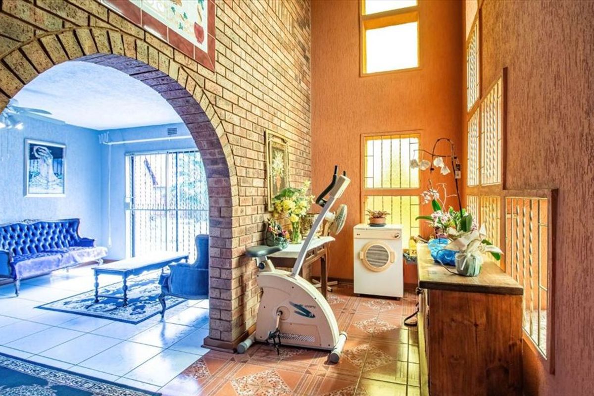 Spacious living area featuring a distinctive brick archway, high ceilings, and tiled flooring, connecting to an adjacent lounge space.