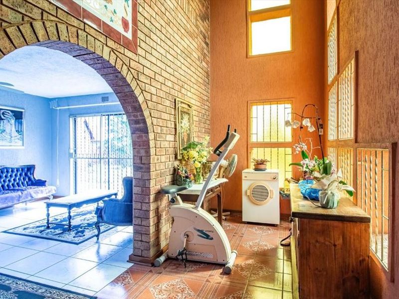 Spacious living area featuring a distinctive brick archway, high ceilings, and tiled flooring, connecting to an adjacent lounge space.